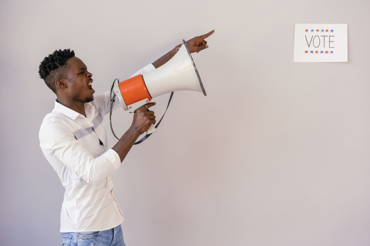 About A passionate man urging people to vote using a megaphone, pointing at a sign.